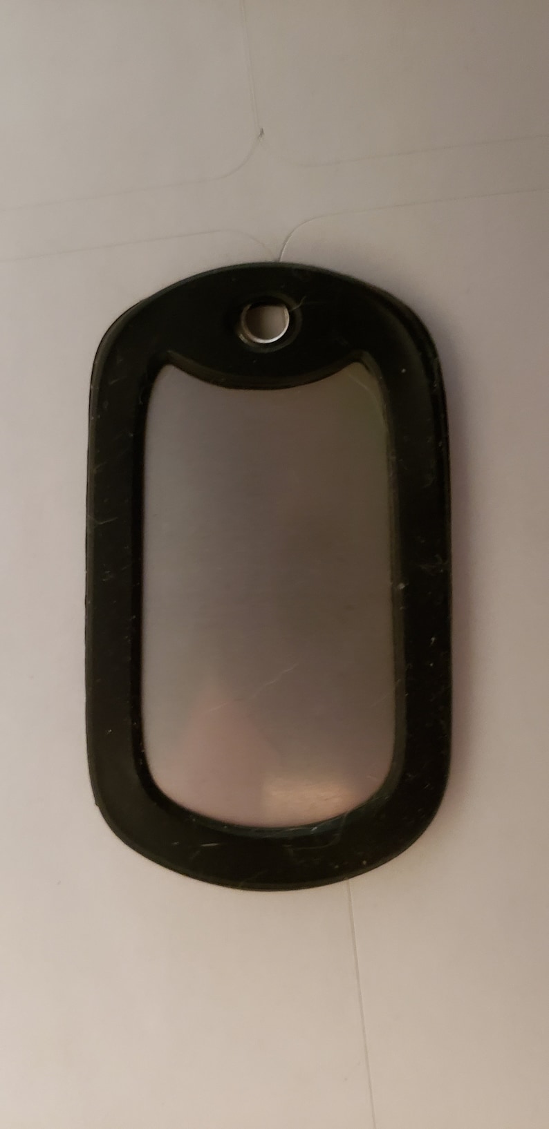 May include: A black dog tag with a silver metal insert. The tag has a round hole at the top for attaching a chain.