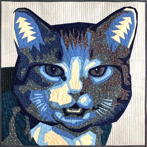 Può includere: Una trapunta blu e bianca a patchwork che raffigura il viso di un gatto. Il gatto ha il naso bianco e uno sfondo a motivi bianco e nero.