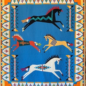 Könnte beinhalten: Eine blaue Decke mit geometrischem Rand und vier stilisierten Pferden in verschiedenen Farben. Die Pferde sind schwarz, rot, weiß und gelb.
