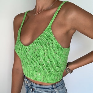 May include: A bright green knitted crop top with a scoop neckline and thin straps. The top has a textured appearance with flecks of white and pink. The bottom hem is ribbed. This handmade top is perfect for summer.