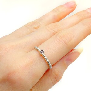 May include: A silver ring with a beaded band and a small purple gemstone in the centre.