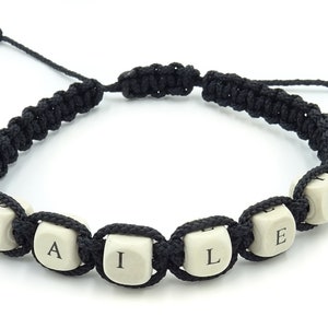 May include: Black macrame bracelet with the name "BAILEY" spelled out in white cube beads. The bracelet is adjustable and features a sliding knot closure. The beads have black letters.