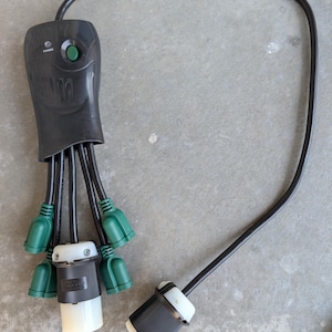May include: A black power adapter with multiple green-tipped outlets and a single plug. The adapter has a green power button and a black cord. The outlets are designed to accommodate various electrical devices.