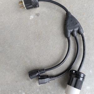May include: A black electrical adapter with a three-way splitter. The adapter has a male plug on one end and two female connectors and a single female connector on the other end. The connectors are black and white.