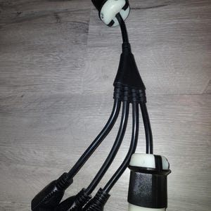 May include: A black electrical adapter with four black plugs on one end and a white plug on the other end.