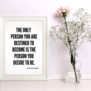 A bold, minimalistic art print sits against a wall next to a flower. The print features a literary quote in bold, black letters, fitting most decor. The quote is motivational and by famed poet Ralph Waldo Emerson.