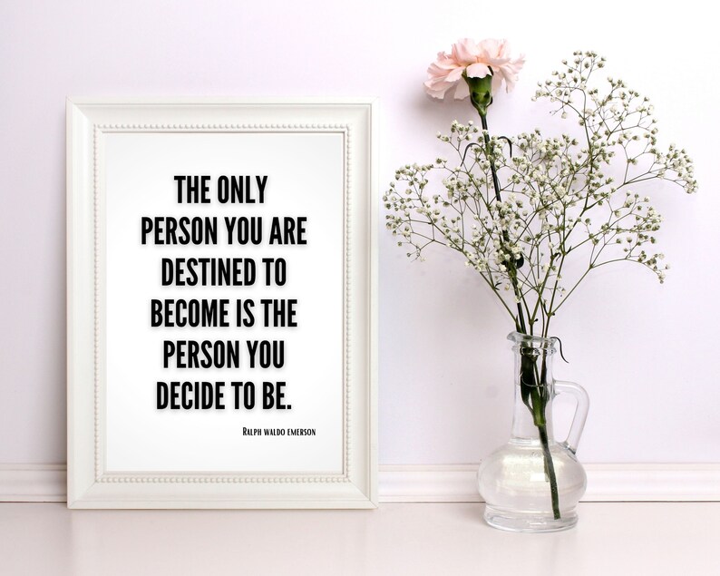 A bold, minimalistic art print sits against a wall next to a flower. The print features a literary quote in bold, black letters, fitting most decor. The quote is motivational and by famed poet Ralph Waldo Emerson.