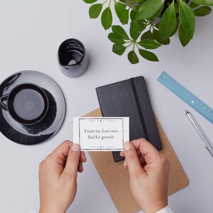 A growth mantra is held in the hands of someone overlooking a desk with coffee, a notebook, a plant, a ruler, and pen.