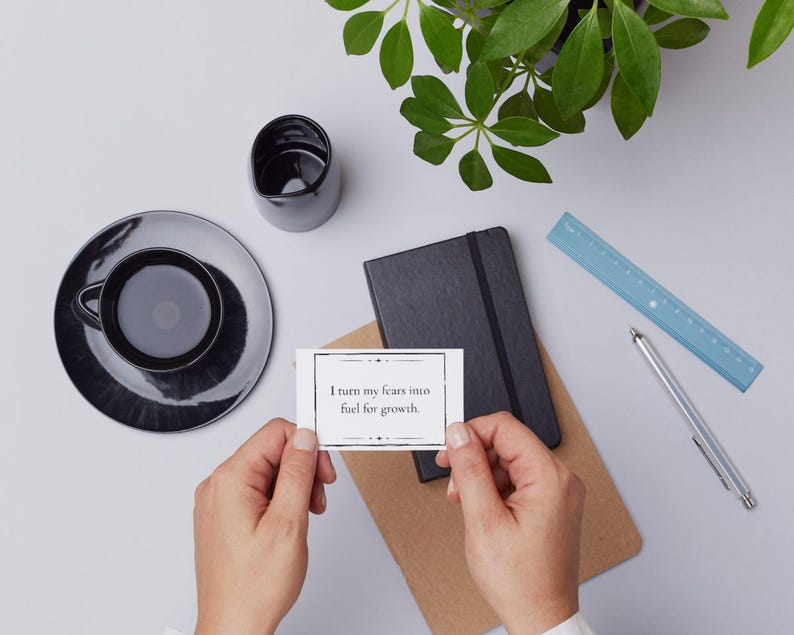 A growth mantra is held in the hands of someone overlooking a desk with coffee, a notebook, a plant, a ruler, and pen.