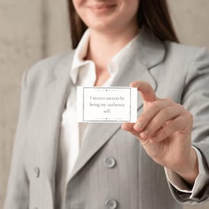 A woman dressed in a business suit holds a mantra card about attracting success.