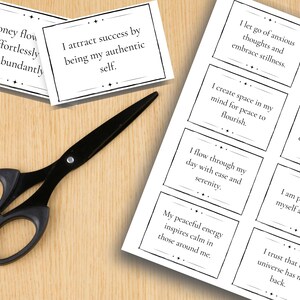 A sheet of daily affirmation mantras is shown on what looks like a desk with a pair of scissors and two individual cards cut out.