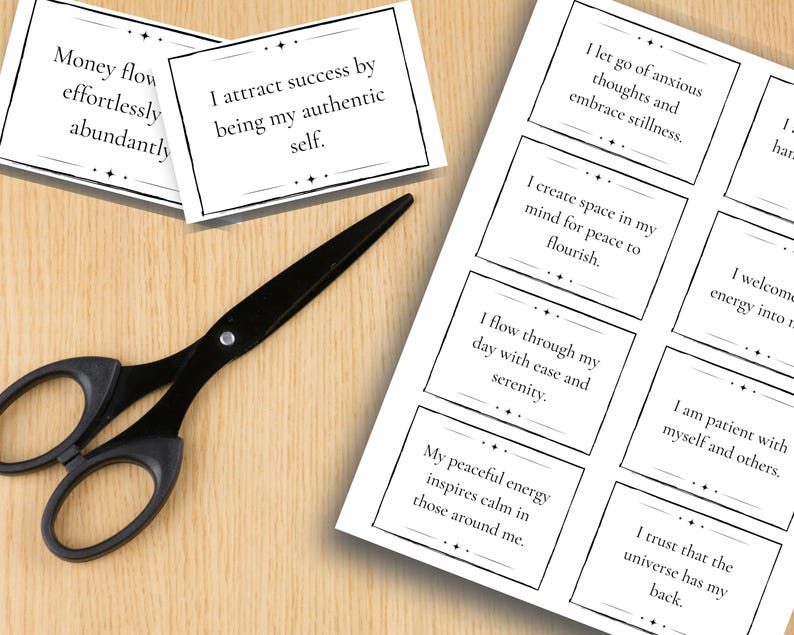 A sheet of daily affirmation mantras is shown on what looks like a desk with a pair of scissors and two individual cards cut out.