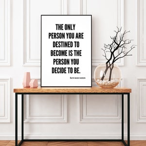 A motivational art print featuring a literary quote from Ralph Waldo Emerson sits on a decorative table in a home. The only person you are destined to become is the person you decide to be. Ralph Waldo Emerson.