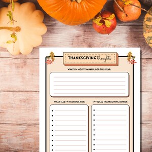 Thanksgiving Thoughts printable writing prompt sheet is shown on a light wooden table with bright orange pumpkins and autumn fruits.