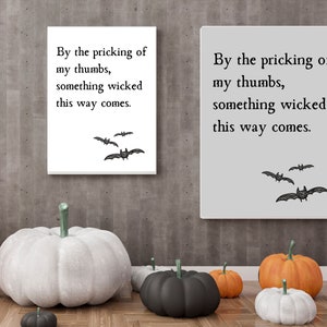 Two quote art prints, one in white and one in gray, hang next to each other on a wall above some pumpkins, making for great Halloween decorations. Something wicked this way comes quote from Macbeth is featured with minimalistic design.