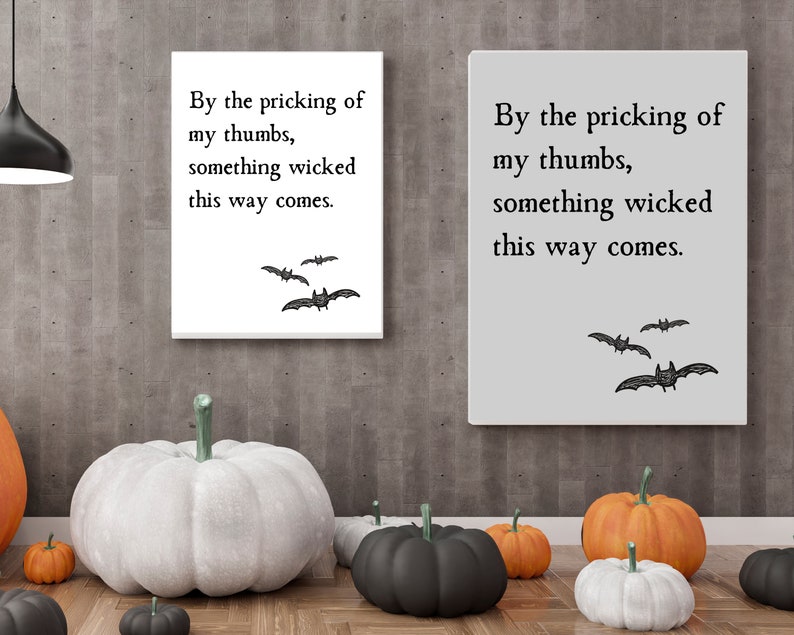 Two quote art prints, one in white and one in gray, hang next to each other on a wall above some pumpkins, making for great Halloween decorations. Something wicked this way comes quote from Macbeth is featured with minimalistic design.