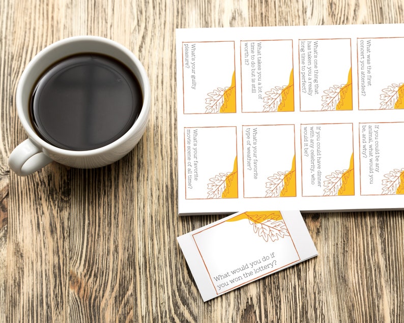 A sheet of Thanksgiving conversation starter cards sits next to a cup of coffee on a table.