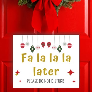 Fa la la la later, Please do not disturb written on a Christmas door sign with ornaments. The paper sign is against a red door with a christmas wreath.