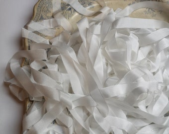 May include: A collection of white silk ribbons, loosely arranged on a decorative plate. The ribbons are a bright white color, with a slight sheen. The plate has a scalloped edge and a blue floral pattern.