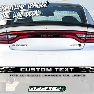 May include: White car with a custom flame tail light decal. The decal features the text "HEAT" in red, with flame graphics. The bottom of the car has a black and white flame design with the text "CUSTOM TEXT". The decal fits 2015-2022 Charger tail lights.