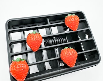 May include: Five red plastic strawberries with green leaves are placed on a black plastic car air vent.