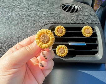 May include: Five yellow sunflower car air freshener clips. One sunflower is being held in a hand with leopard print nail polish.