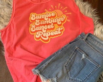 May include: A coral pink tank top with a graphic design that says "Sunrise Sunburn Sunset Repeat" in a retro font with a yellow sun graphic.