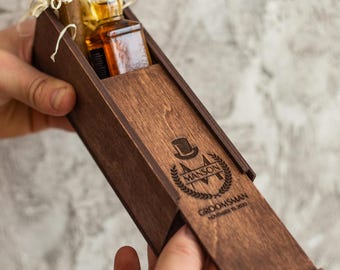 May include: A wooden box with a sliding lid, engraved with the text "Manson,  Groomsman, November 15, 2020". The box contains a small bottle of liquor and a cigar.
