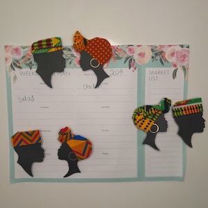 May include: A weekly planner with floral accents and several decorative silhouette magnets. The magnets depict profiles wearing colorful head wraps and hats. The planner includes sections for meal planning and a market list.