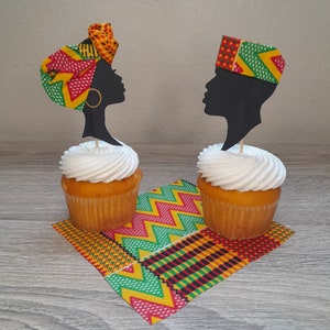 May include: Two cupcakes with white frosting topped with black silhouette cupcake toppers. The topper on the left is a woman wearing a colorful head wrap. The topper on the right is a man wearing a colorful hat. The cupcakes are on a colorful patterned napkin.
