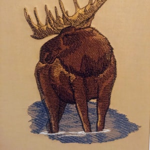 May include: Embroidered image of a brown moose with large antlers standing in water. The moose is facing away from the viewer, with its back and hind legs visible.