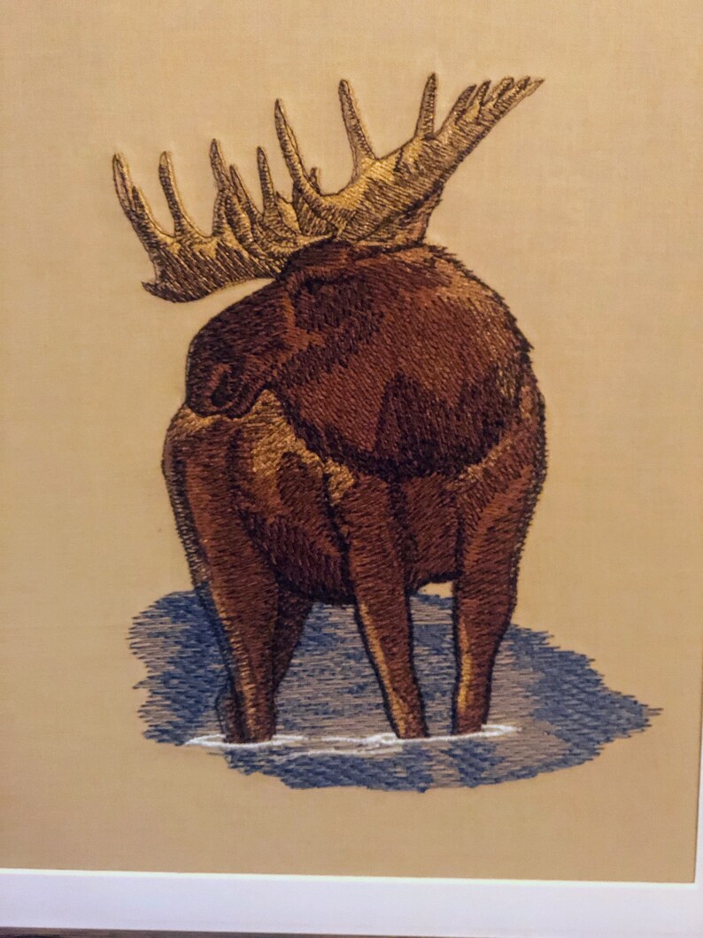 May include: Embroidered image of a brown moose with large antlers standing in water. The moose is facing away from the viewer, with its back and hind legs visible.