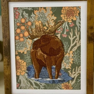 May include: Embroidered moose standing on a blue background with a floral pattern. The moose is brown and has large antlers.