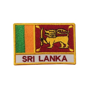 May include: An embroidered patch featuring the flag of Sri Lanka. The patch is rectangular and has a gold border. The flag is red with a yellow lion holding a sword, and a green and orange vertical stripe on the left side. The words "SRI LANKA" are embroidered in gold on a white background at the bottom of the patch.