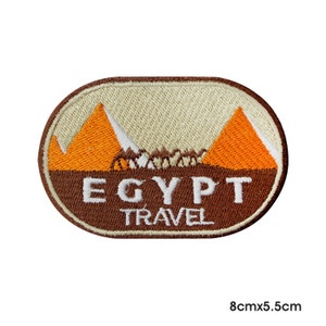 Peut inclure: Patch brodé avec une bordure ovale marron. Le centre présente un fond beige avec deux pyramides orange et le texte "EGYPT TRAVEL" en blanc.