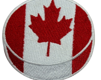 May include: A round white and red embroidered patch with the Canadian flag. The patch features a red maple leaf on a white background with a red stripe on each side.