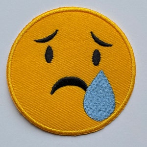 May include: Yellow embroidered patch with a sad face emoji with a single blue teardrop.