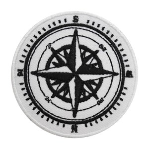 May include: A white embroidered patch with a black compass design. The compass has a star in the center with four points and a circle around it with the cardinal directions marked.