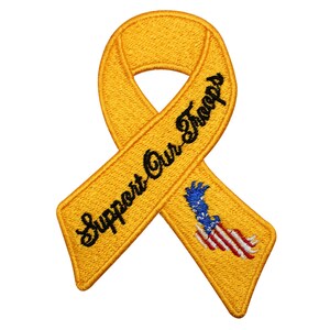 Könnte beinhalten: Gelbes Band mit dem Text "Support Our Troops" in schwarzer Stickerei. Das Band hat eine kleine gestickte amerikanische Flagge in der Mitte.