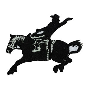 May include: Black silhouette of a cowboy riding a bucking horse. The cowboy is wearing a hat and has his arms outstretched. The horse is rearing up on its hind legs. The image is a simple, stylized design.