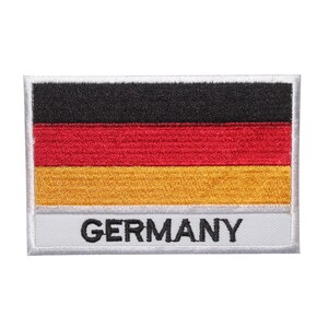 May include: A black, red, and yellow embroidered patch with the word "GERMANY" in black lettering on a white background.