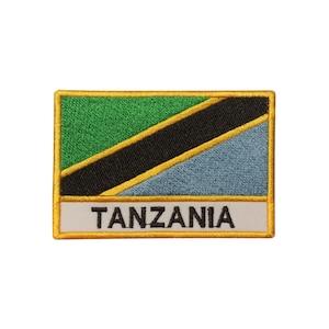 May include: An embroidered patch with the Tanzanian flag. The flag is green, black, yellow, and blue. The patch has a gold border and the word "TANZANIA" is written in black on a white background.