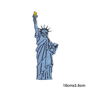 May include: Blue embroidered patch of the Statue of Liberty holding a torch and a book. The patch is 10cm by 3.5cm.