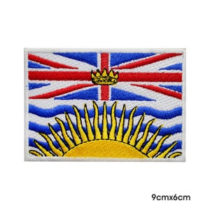 Könnte beinhalten: Ein gestickter Aufnäher mit der Flagge von British Columbia. Der Aufnäher ist weiß mit einem blauen und roten Union Jack in der oberen Hälfte und einer gelben Sonne mit blauen Wellen in der unteren Hälfte. Der Aufnäher misst 9 cm x 6 cm.