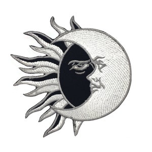 May include: A black and white embroidered patch featuring a sun and moon design. The sun has a stylised face with a single eye and the moon is a crescent shape.