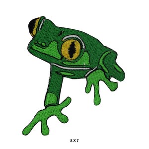 Könnte beinhalten: Grüner gestickter Frosch-Patch mit einem gelben Auge. Der Frosch befindet sich in einer Sprunghaltung mit ausgestreckten Beinen. Der Patch ist 8 Zoll mal 7 Zoll groß.