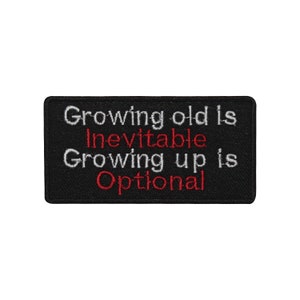 May include: A black rectangular patch with white and red embroidered text. The text reads "Growing old is Inevitable Growing up is Optional". The patch is designed to be sewn or ironed onto clothing or accessories.