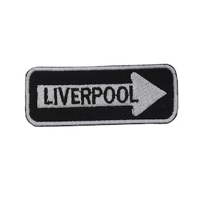 May include: Black and white embroidered patch with a white arrow pointing to the right and the word "LIVERPOOL" in black text.