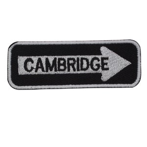 May include: Black and white embroidered patch with a white arrow pointing to the right and the word "CAMBRIDGE" in black.