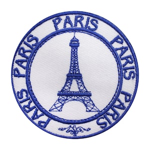May include: A white circular embroidered patch with a blue outline. The patch features a blue silhouette of the Eiffel Tower and the word "PARIS" repeated four times around the edge.